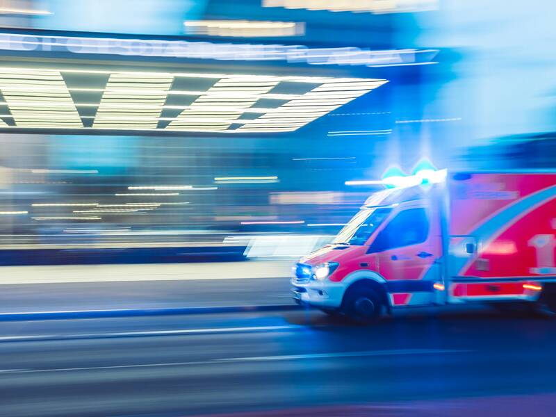 Ein Krankenwagen mit eingeschaltetem Blaulicht fährt schnell eine belebte Straße entlang.