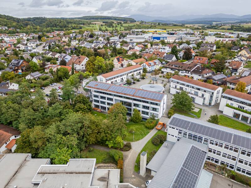 Das Bild zeigt eine Luftaufnahme von Efrinen-Kirchen mit verschiedenen Gebäuden, darunter ein paar mit Solarpaneelen auf den Dächern, umgeben von grüner Landschaft.